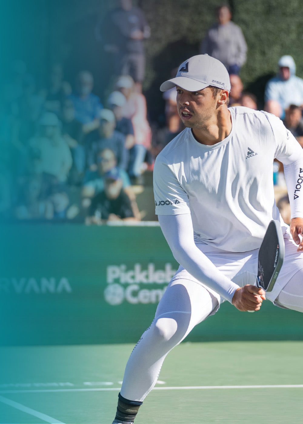 Mann in weißer Sportkleidung und Cap spielt Pickleball mit Schläger auf Outdoor-Court vor Zuschauern.